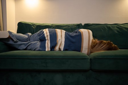 Cozy solitude with woman resting on sofa under soft evening lightの写真素材