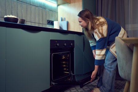 Focused woman checking meal in oven during mindful cooking routineの写真素材