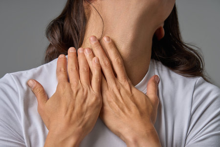 Close-up of woman touching her neck with both hands showing pain and discomfort