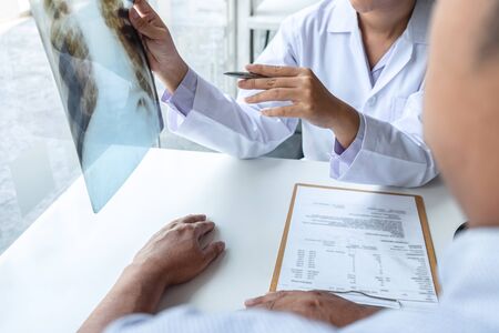 Doctor holding and looking at x-ray film examining at lungs radiograph of patient chest injury and analyze result while discussing explaining problem of medical.の写真素材
