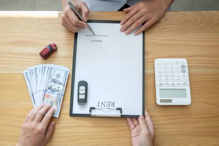 Car rental and Insurance concept, Young salesman receiving money and giving car's key to customer after sign agreement contract with approved good deal for rent or purchase.の写真素材