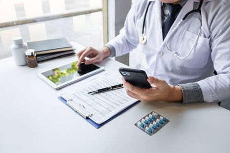 Doctor working and using smartphone note information on paper report in hospital and medical stethoscope, medicine on clipboard on desk.の写真素材