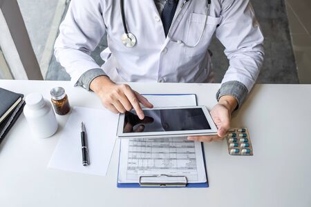 Doctor working and using digital tablet note information on paper report in hospital and medical stethoscope, medicine on clipboard on desk.の写真素材