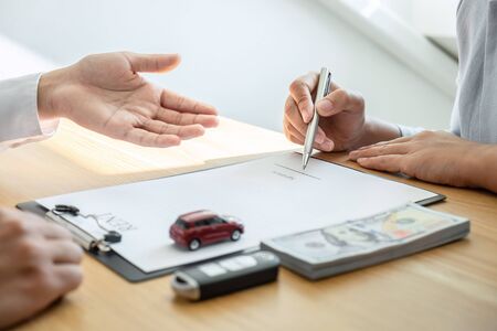 Car rental and Insurance concept, Young salesman presenting and pointing signature form to customer signing after decision sign agreement contract with approved good deal for rent or purchase.の写真素材
