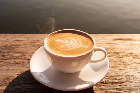 Close up a coffee latte in white cup and milk froth above to drink on brown wooden table background, increase energy for today.の写真素材