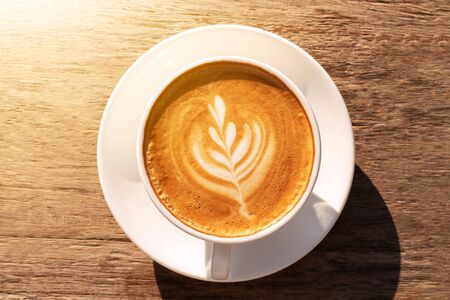 Close up a coffee latte in white cup and milk froth above to drink on brown wooden table background,...