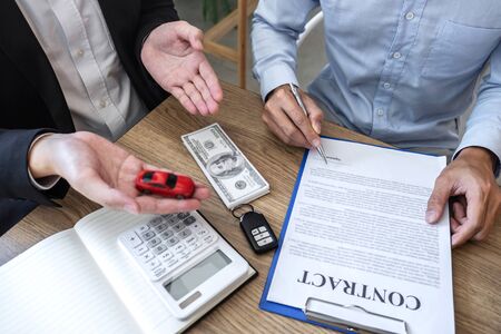 Car rental and Insurance concept, Young salesman giving car's key to customer after sign agreement contract with approved for rent or purchase.の写真素材