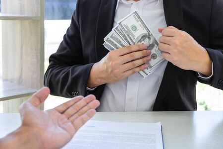 Businessman giving bribe money in the envelope of their partner to give success the deal contract in...