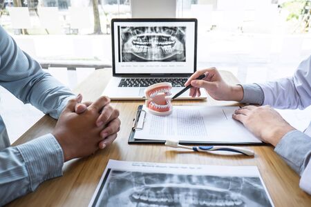 Professional Dentist and patient discussing jaw and teeth the x-ray photograph during explaining the consultation treatment issues and writing patient history list on note pad.の写真素材