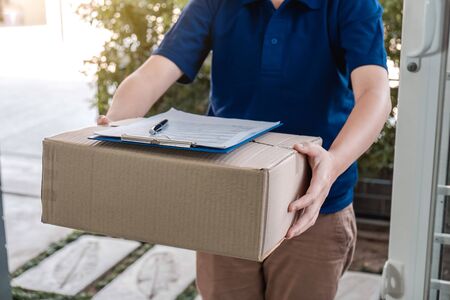 Delivery man deliver box parcel package and clipboard documents sending to customer in front of the house.の写真素材