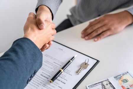 Real estate agent are shaking hands after good deal and giving house, keys to customer after signing...
