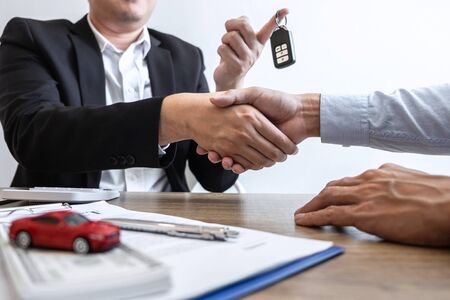 Car rental and Insurance concept, Young salesman shaking hands after finishing up a collaboration discussing with customer after sign agreement contract with approved good deal for rent or purchase.の写真素材
