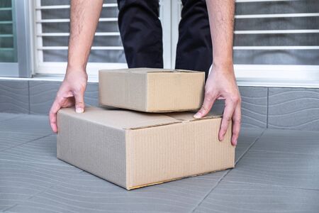 Man's hand holding boxes at the front door to receive package, shipping delivery concept.