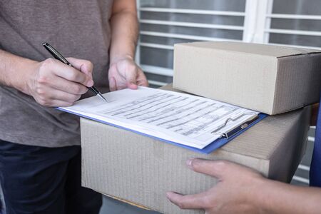 Young Delivery man deliver box parcel package and sending to customer in front of the house, Man customer signing in clipboard form to receive package, shipping delivery concept.の写真素材
