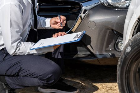 Insurance Agent Inspecting assessed Damaged Car checking and signing on report insurance claim form...