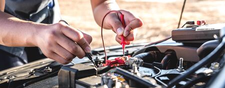 Mechanic repairman checking engine automotive in auto repair service and using digital multimeter testing battery to measure various values and analyze.の写真素材