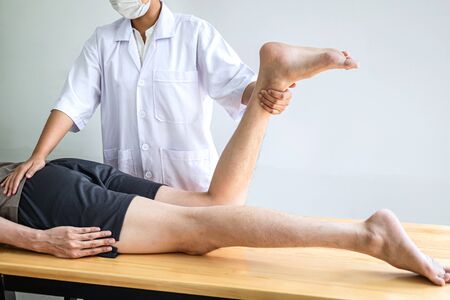 Female Physiotherapist working examining treating injured leg of male patient, Doing exercises the...