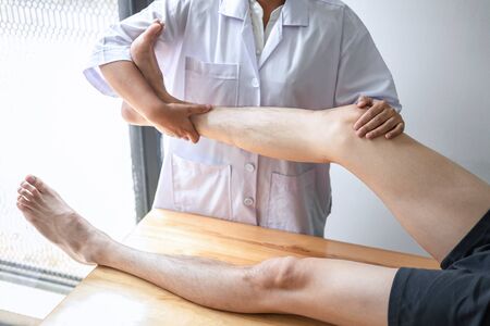 Doctor or Physiotherapist working examining treating injured leg of athlete male patient, Doing the Rehabilitation therapy pain in clinic.の写真素材