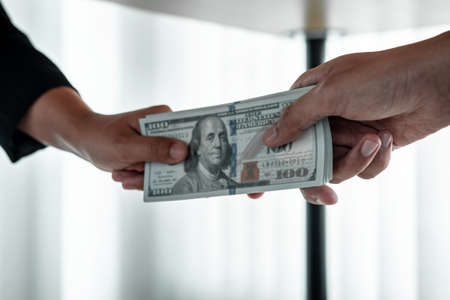 Business people giving bribe money under table to hand of their partner to give success the deal contract in a corruption, illegal and dishonest.の写真素材