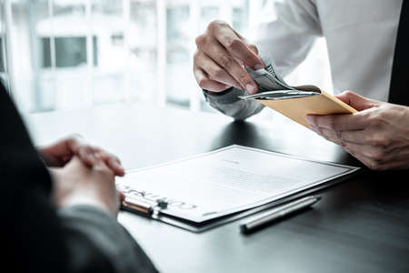 Businessman giving bribe money in the envelope to businesswoman to bribing deal contract in a corruption, Illegal, dishonest and scam.の写真素材