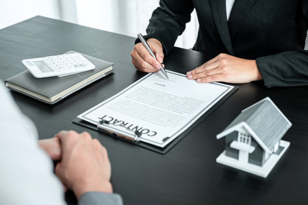 Real estate agent working sign agreement document contract for home loan insurance approving purchases for client with house model and key on table.の写真素材