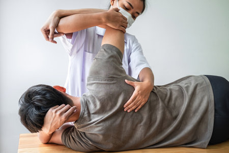 Doctor or Physiotherapist working examining treating injured back of athlete male patient, Doing the Rehabilitation therapy pain in clinic.の写真素材