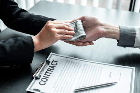 Business woman giving bribe money to businessman to bribing deal contract in a corruption, Illegal, dishonest and scam.の写真素材
