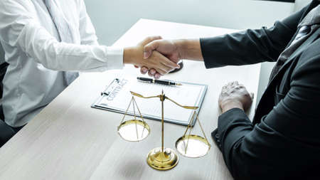 Male lawyer shaking hands with client after good deal negotiation cooperation meeting in courtroom.の写真素材