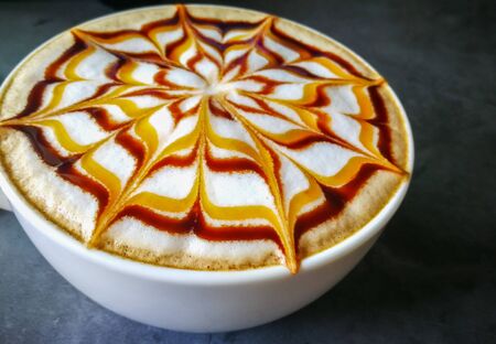 Coffee latte art  caramel and chocolate sauce   with white milk foam  on cement surface work deskの写真素材