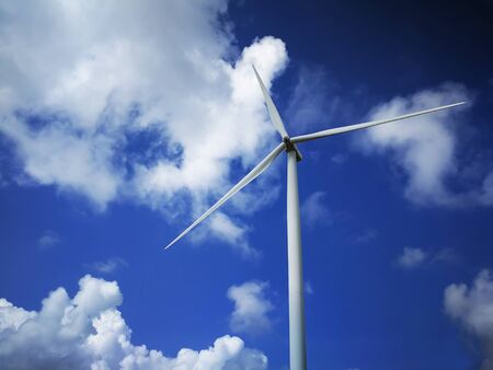 Windmill close up on blue sky and white cloud background. Wind-turbine on wind farm in rotation to...