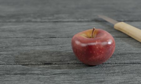 Red apple and blur small knife wood handle on gray wooden surface by 3D renderingの写真素材