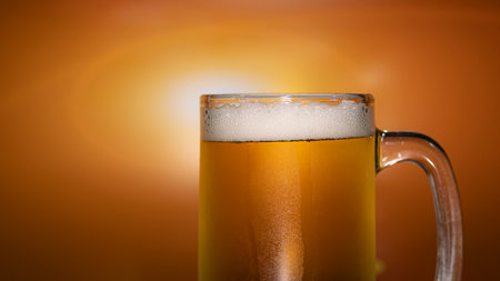 Pour the beer into a clear glass with beer foam and bubble. Golden orange light background.