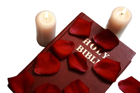 Holy bible with rose petals and two candles on isolated white background