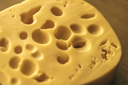 Dutch Hard Cheese Maasdam or Emmentaler Slice Porous Yellow , Cheese with Holes, Swiss Cheese Block Closeupの写真素材