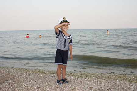 Beautiful 4 year old boy smiling and posing in captains hat against the background of the sea.の写真素材