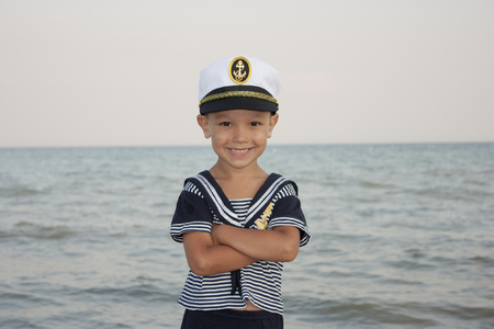 Beautiful 4 year old boy smiling and posing in captains hat against the background of the sea.の写真素材