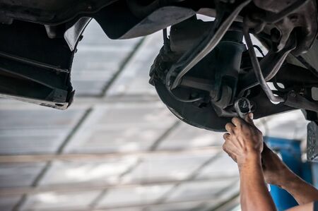 Auto mechanic asian checking bush-bolt under double wishbone suspension by hand with tools car liftの写真素材