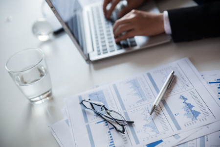 Businessman checking reported profits on the paper and laptop.