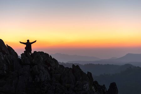 silhouette of a standing man on top of a cliff mountain with arms raised during sunset celebrate success - landscape sunset Thailandの写真素材