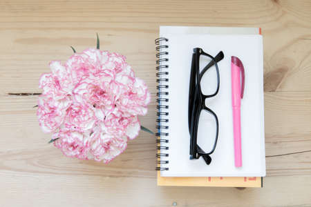 notebook, book, pen with glasses and carnation flowers on wooden table,  top view.の写真素材