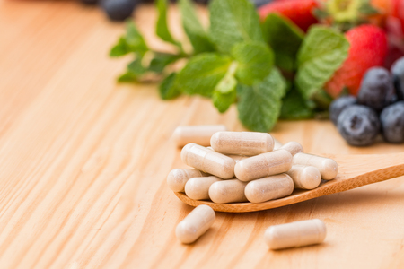 Vitamins supplements in spoon on wooden table.の写真素材