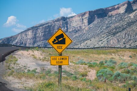 Sign of traffic alerts downhill slope 10 %, reduce speed and use a lower gear. Drive with caution.の写真素材