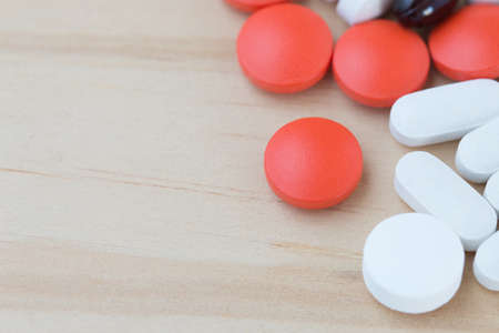White, black and red medicine pills on a wooden background.