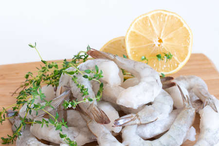 Frozen raw shrimps peeled on a wooden cutting board with herbs and lemon.の写真素材