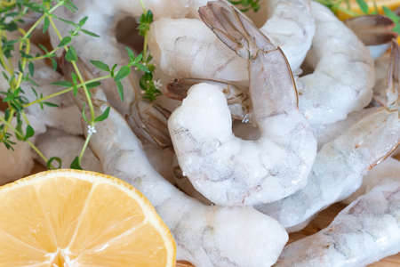 Frozen raw shrimps peeled on a wooden cutting board with herbs and lemon.の写真素材