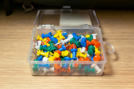 Colorful pushpins in a plastic box on a wooden table.の写真素材