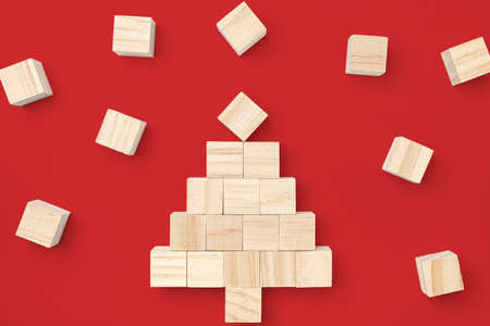 Wooden cube block stacking into a Christmas tree surrounded by small wooden cubes isolated on red...