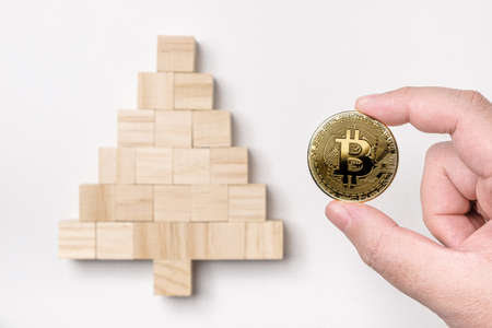 Hand putting bitcoin on top of wooden cube block stacking into a Christmas tree isolated on white...