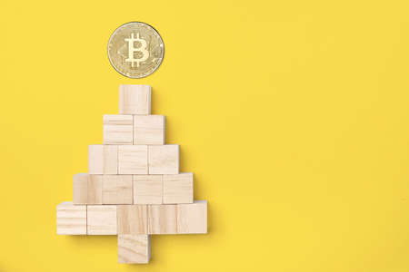 Wooden cube block stacking into a Christmas tree with bitcoin on top isolated on yellow background, concept of Christmas, happy new year, bitcoin, cryptocurrencyの写真素材