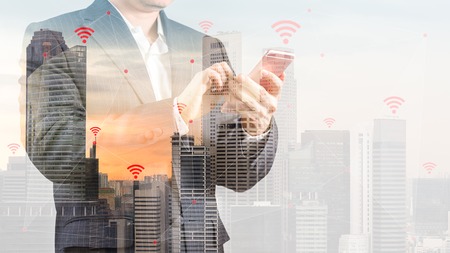 Double Exposure of City Background with Businessman in Suit Using Smartphone Illustrating Wireless...